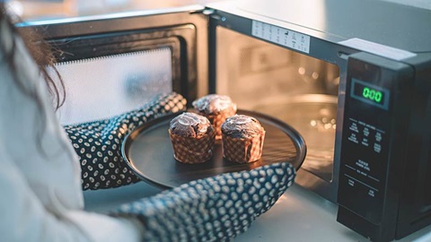 Une femme met des gâteaux au micro-ondes avec des gants de cuisine